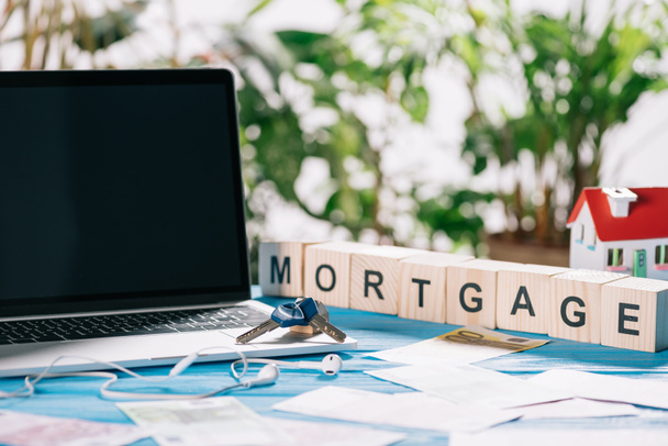 selective focus of laptop with blank screen and keys near headphones, euro banknotes and wooden cubes with letters on desk, mortgage concept - Photo, Image