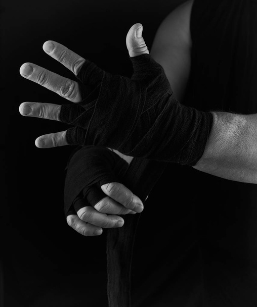 man wraps his hands in black textile bandage for sports, black white toning - Фото, изображение