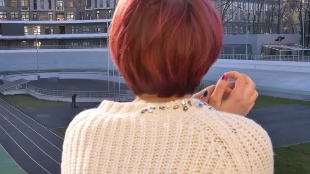 Close-up traseiro-retrato de bela menina de cabelos cor-de-rosa de pé perto de trilhos e atenciosamente assistindo em vista urbanística
. - Filmagem, Vídeo