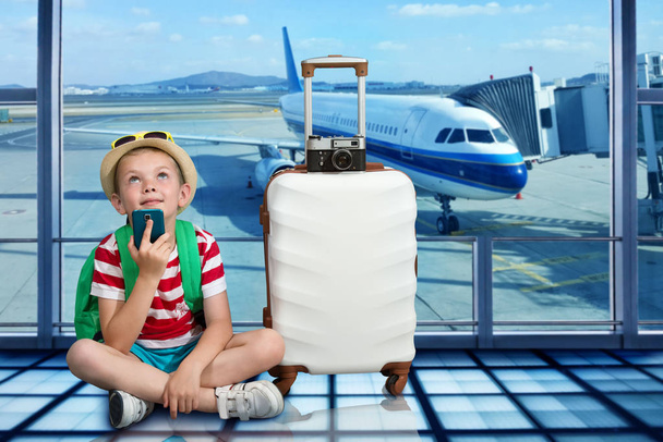 Un ragazzo con una valigia si siede all'aeroporto e aspetta l'atterraggio sull'aereo
. - Foto, immagini