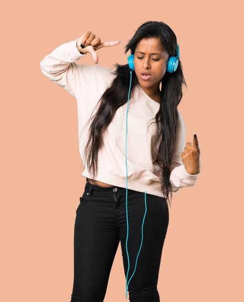 Jeune femme afro-américaine écoutant de la musique avec des écouteurs et dansant sur fond brun isolé
 - Photo, image