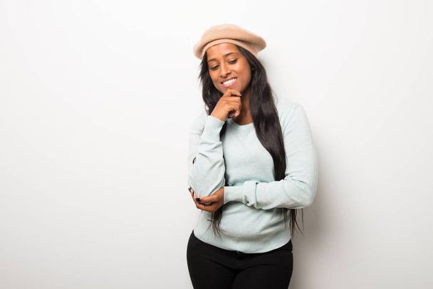 Молодая афро-американка на белой стене смотрит в сторону с рукой на подбородке
 - Фото, изображение