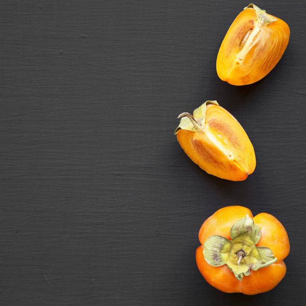 Fresh persimmon on black background, overhead view. Flat lay, overhead, from above. Space for text. - Φωτογραφία, εικόνα