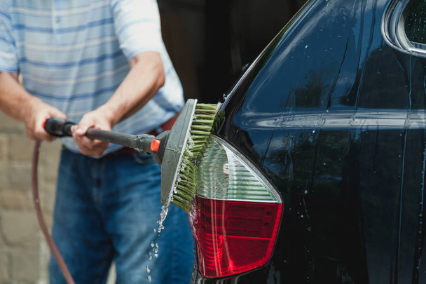 man washes a black car with a special brush on a long handl - Zdjęcie, obraz