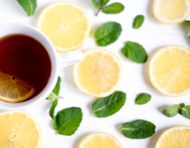A cup of tea along with mint and lemon. Cold tea. Natural cures for the disease. Black tea with lemon on a white background - Fotografie, Obrázek