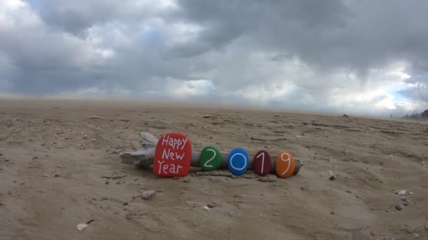 Ευτυχισμένο το νέο έτος πάροδο του χρόνου με ένα χρωματισμένο πέτρες σύνθεση στην παραλία κατά τη διάρκεια μια συννεφιασμένη και θυελλώδη ημέρα - Πλάνα, βίντεο