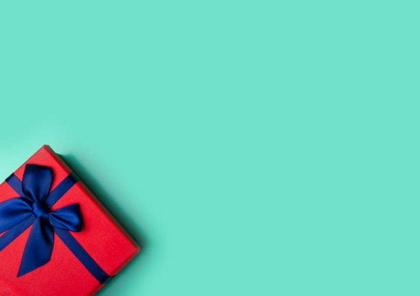 Red box gift with blue ribbon on green background, top view fashion flat lay - Foto, Imagem