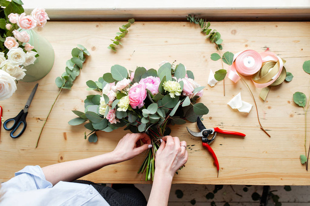 Zbliżenie dłoni profesjonalne kwiaciarni Dokonywanie bukiet róż Jaskier i piwonie w kwiaciarni. Rozmieszczenie i opakowania bukiet. Koncepcja kwiat dostawy i online przechowywania - Zdjęcie, obraz