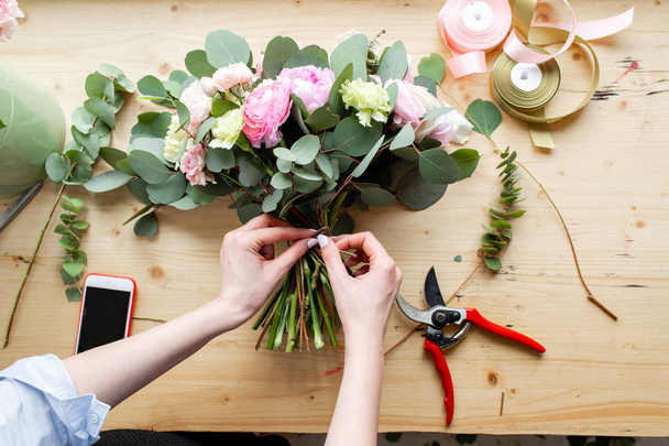 Nahaufnahme einer professionellen Floristin, die in einem Blumenladen einen Strauß aus rosa Hahnenfuß und Pfingstrosen herstellt. Anordnung und Verpackung des Straußes. das Konzept der Blumenlieferung und des Online-Shops - Foto, Bild