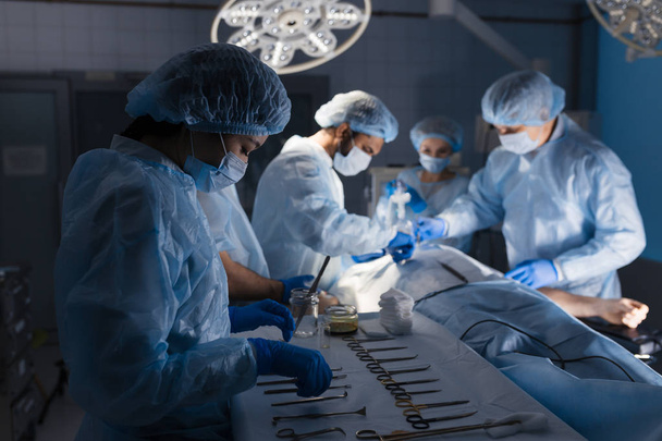 Surgical tools lying on table with nurse near and surgeons at background. - Foto, immagini