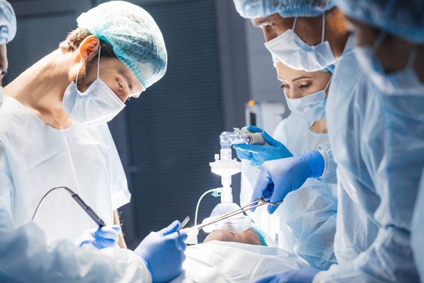Equipo diverso de cirujanos, asistentes y enfermeras que realizan cirugía invasiva - Foto, Imagen