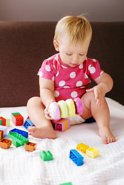 Χαριτωμένο μωρό κορίτσι παίζει με πολύχρωμο πλαστικό μπλοκ σε εσωτερικούς χώρους - Φωτογραφία, εικόνα