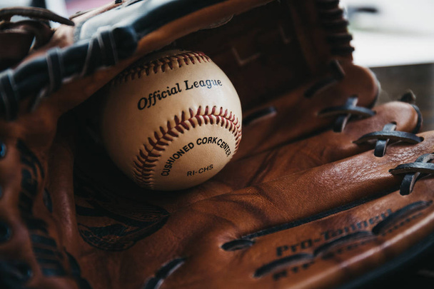 Londres, Reino Unido - 3 de enero de 2019: Primer plano de una pelota de béisbol blanca dentro del guante de béisbol bronceado. El béisbol, originario de Inglaterra en el siglo XVIII, es un deporte muy popular en muchos países del mundo.
. - Foto, Imagen