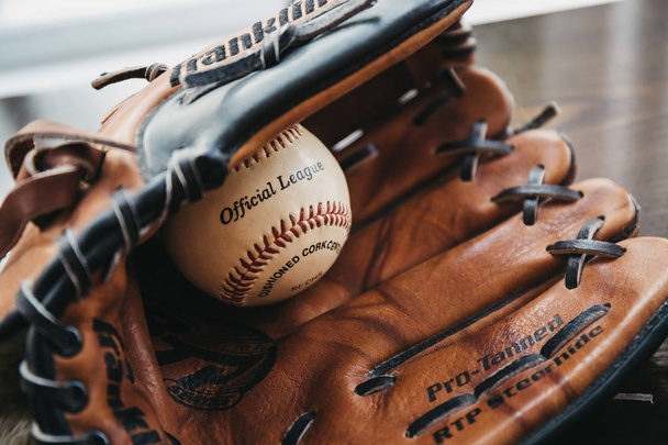 Londres, Reino Unido - 3 de enero de 2019: Primer plano de una pelota de béisbol blanca dentro del guante de béisbol bronceado. El béisbol, originario de Inglaterra en el siglo XVIII, es un deporte muy popular en muchos países del mundo.
. - Foto, imagen