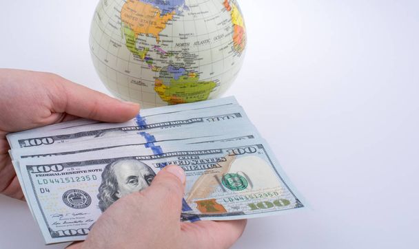 Ludzka dłoń trzymająca amerykańskie banknoty dolarowe obok modelowego globu na białym tle - Zdjęcie, obraz