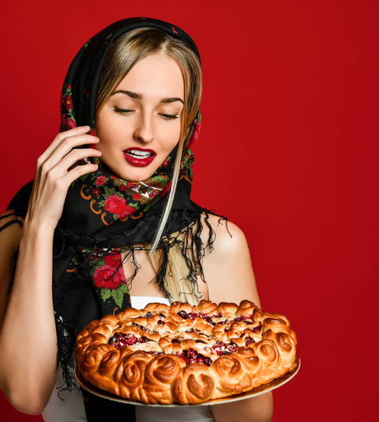 Portrait of a young beautiful blonde in headscarf holding a delicious homemade cherry pie. - Fotoğraf, Görsel