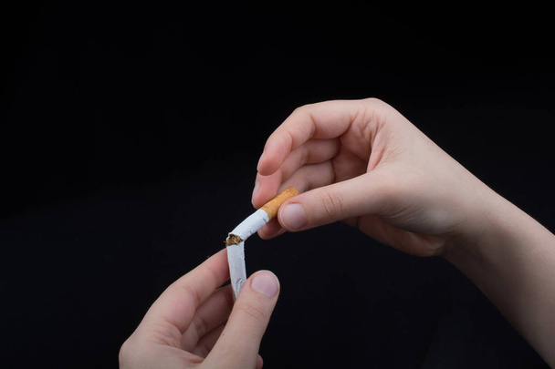 La mano está rompiendo un cigarrillo sobre un fondo negro - Foto, Imagen