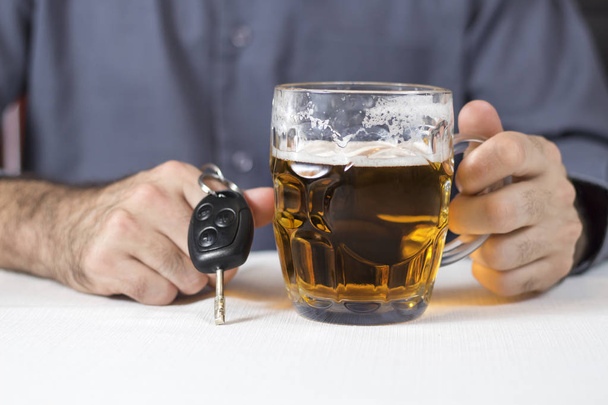 Η αρσενική χέρι κρατά μια κούπα μπύρα. Το άλλο χέρι κρατά τα κλειδιά του αυτοκινήτου. - Φωτογραφία, εικόνα