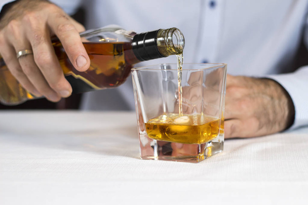 男性の手は、氷の入ったグラスにボトルからウイスキーを注ぐ. - 写真・画像