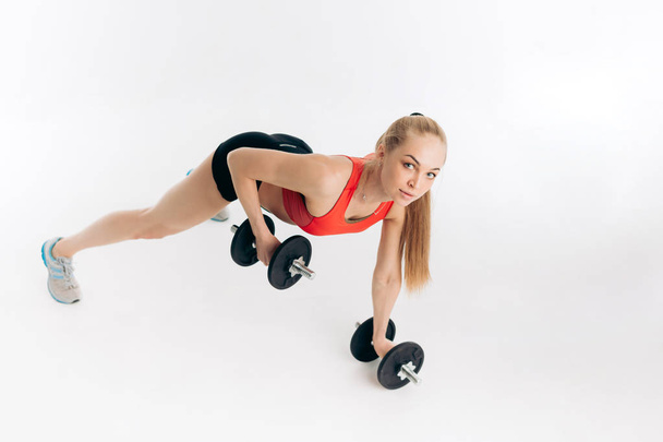 positive blonde sportswoman is training with dumbbells and looking at the camera. full length photo. - Foto, Bild