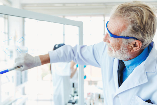 Professeur de sciences hommes travaillant avec des produits chimiques de panneau de verre transparent dans le laboratoire
 - Photo, image