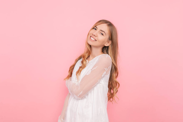 Happy girl with curled hair in a white dress on a pink background - Photo, Image