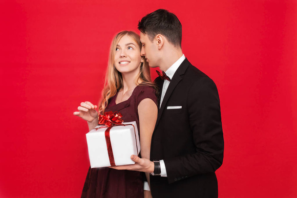 An elegant man in a suit gives a surprise to a woman, gives her a gift, on a red background - Фото, изображение