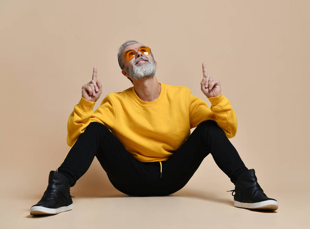 Portrait of gray hair senior millionaire man in yellow sunglasses pointing fingers up - Photo, Image