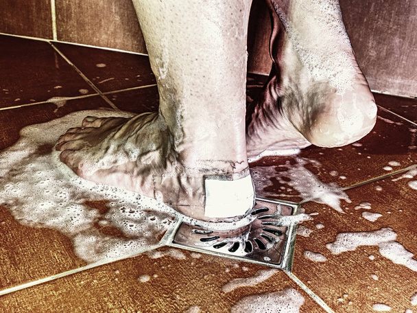 Secousses avec peau douloureuse à pied avec du plâtre adhésif. Corps féminin prenant douche dans la salle de bain moderne carrelée
. - Photo, image