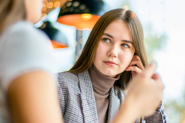 A girl in turtleneck with hand near her head is looking attentively to a friend during conversation. - Foto, afbeelding