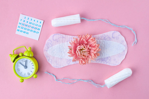 Tampons for menstruation, alarm clock, women's calendar, feminine pads and a pink flower on a pink background. Hygiene care during critical days. Regular menstrual cycle.  - Fotoğraf, Görsel