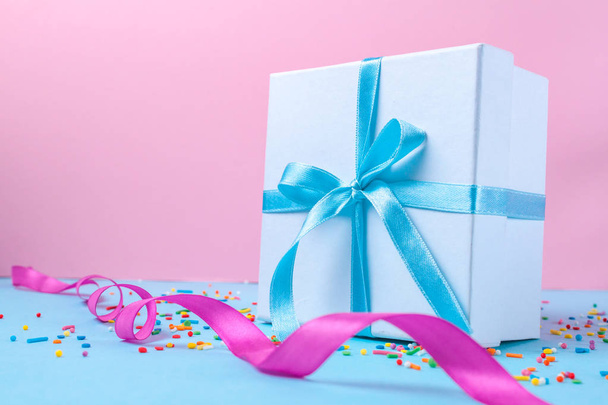 Gift, small box tied with a satin blue ribbon on a pink background. Gift concept. Surprises and gifts for loved ones, congratulations on holidays, give gifts. Copy space  - Фото, зображення