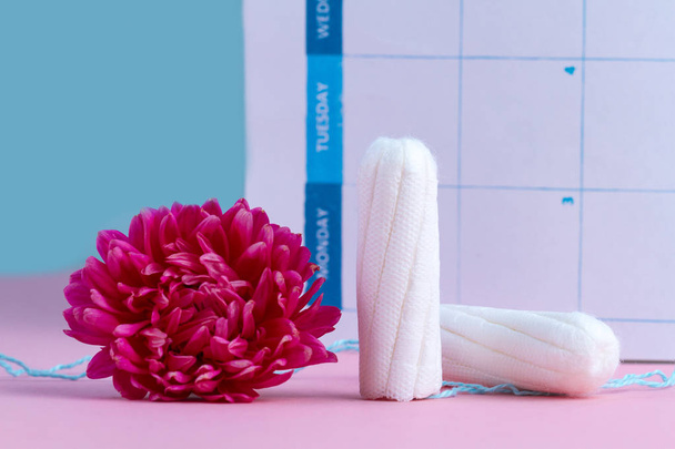 Tampons for critical days and a pink flower on a pink background. Hygiene care during menstruation. Regular menstrual cycle. Caring for women's health. - 写真・画像