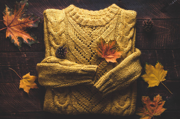 温かみのあるニットのセーターと木製の背景の秋のカエデの葉。秋の服  - 写真・画像