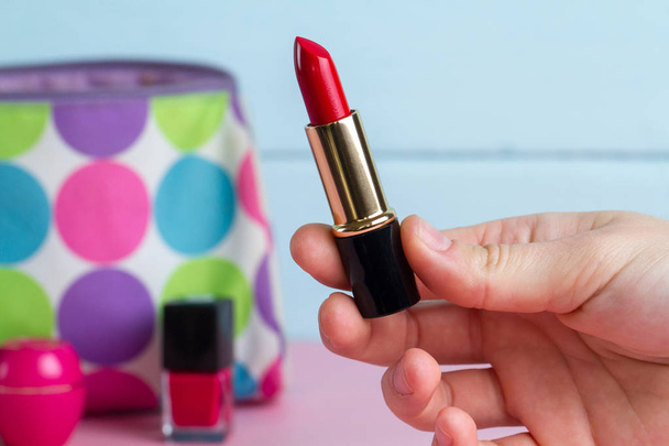 A woman holds red lipstick in the hands against the background of women's cosmetic bag. Women's accessories, cosmetics - Foto, Imagem