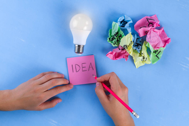 Idea concept. New idea. Colorful crumpled paper balls, notebook and light bulb on a blue background. Start up. Copy space  - Foto, immagini