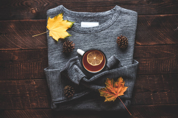 Теплий светр, соснові шишки, чашка гарячого чаю з лимонним і осіннім кленовим листям на дерев'яному тлі. Осінній одяг
.  - Фото, зображення