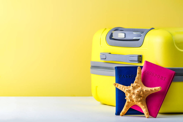 A bright, yellow travel suitcase, passport and starfish on a yellow background. Travel concept. Copy space  - Valokuva, kuva