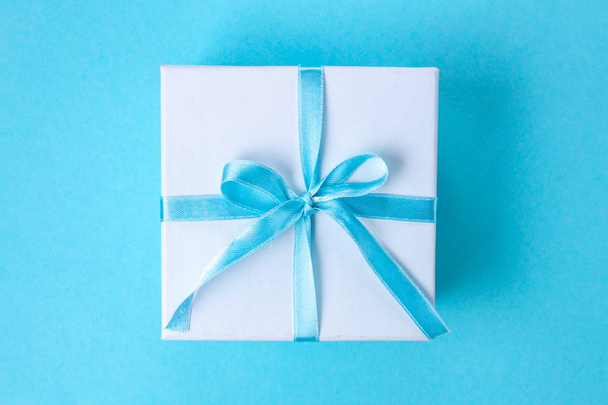 Подарок, маленькая коробочка, связанная атласной голубой лентой на синем фоне. Концепция подарков. Сюрпризы и подарки для близких
 - Фото, изображение