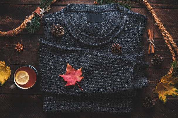 Warm sweater, pine cones, a mug of hot tea with lemon, cinnamon and aniseed stars and autumn maple leaves on a wooden background. Autumn clothes and drinks. Autumn concept.  - Fotoğraf, Görsel