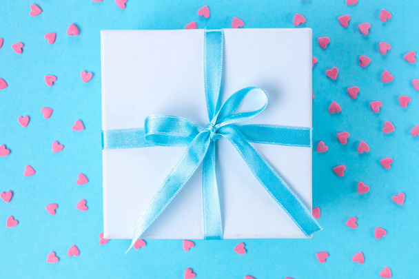 Gift, small box tied with a satin blue ribbon on a blue background. Gift concept. Surprises and gifts for loved ones - Фото, изображение