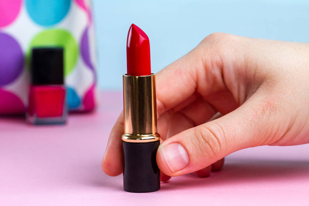 A woman holds red lipstick in the hands against the background of women's cosmetic bag. Women's accessories, cosmetics for makeup - 写真・画像
