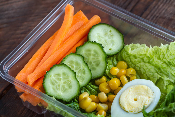 Healthy meal in a plastic container. Snack in the office, at work. Lunch box of cucumbers, buckwheat, carrots, eggs, lettuce and canned corn. Nutrition and healthy food concept - Photo, Image