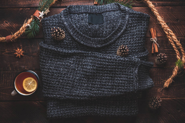 Warm sweater, pine cones, a mug of hot tea with lemon, cinnamon and aniseed stars on a wooden background. Winter clothes and drinks. Winter concept.  - Photo, image