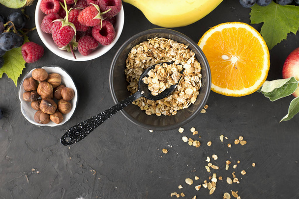 Healthy food. Ingredients for the preparation of breakfast food. Granola, grapes, blueberries, oranges, nuts, seeds, apple, banana. Balanced nutrition of the whole family. Top view on a dark background. - Photo, image