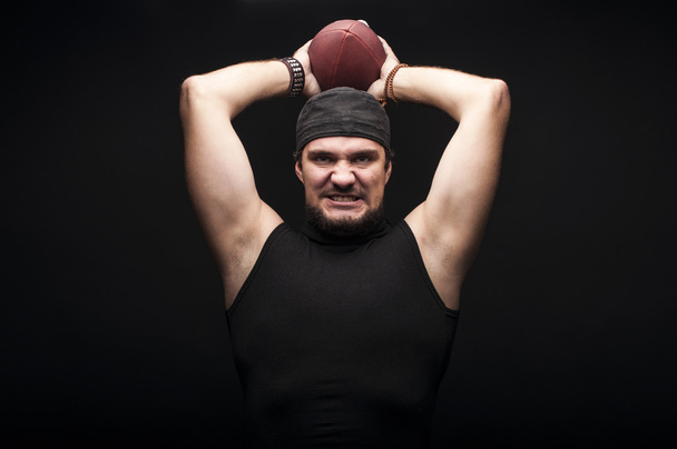 American football speler in studio met bal op zwarte achtergrond - Foto, afbeelding