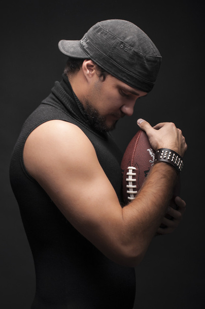 αμερικανικός παίκτης ποδοσφαίρου στο στούντιο με μπάλα σε μαύρο φόντο - Φωτογραφία, εικόνα