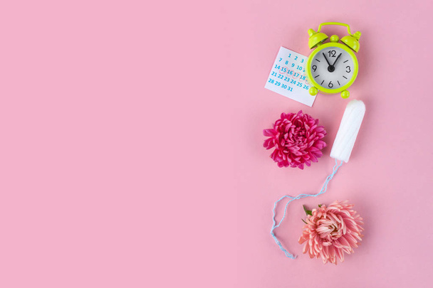 Tampons for menstruation, alarm clock, women's calendar and a pink flower on a pink background. Hygiene care during critical days. Regular menstrual cycle. Copy space  - Фото, изображение
