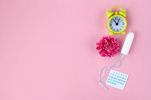 Tampons for menstruation, alarm clock, women's calendar and a pink flower on a pink background. Hygiene care during critical days. Regular menstrual cycle. Copy space  - Photo, image