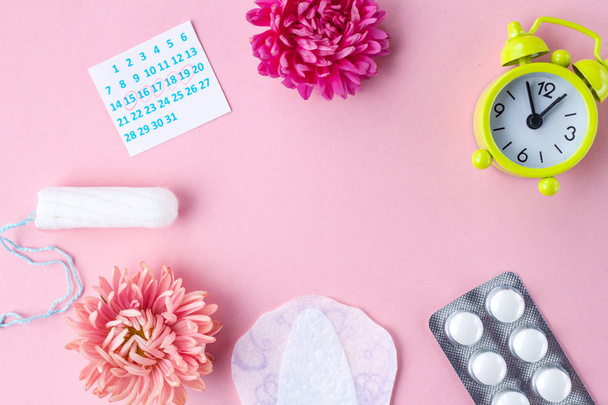 Tampons for menstruation, alarm clock, women's calendar, feminine pads, pain pills for critical days and flowers on a pink background. Hygiene care during critical days. Regular menstrual cycle. Copy space  - Photo, Image